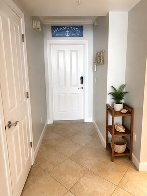 A hallway with a white door, a sign reading 'ISLAMORADA,' and a wooden shelf with decorative items. - Waterfront Condo in Heart of Islamorada, Boat slip (Islamorada)