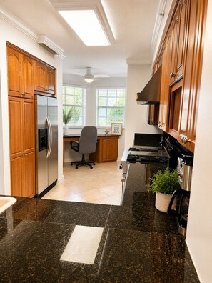 A kitchen with wooden cabinets, a stainless steel refrigerator, a stove, and a window with a view of greenery. - Waterfront Condo in Heart of Islamorada, Boat slip (Islamorada)