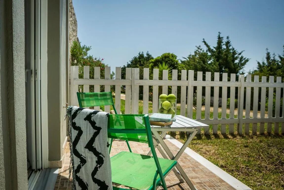 Een terras met een witte picket-omheining, groene stoelen, een klein tafeltje en een mand appels.