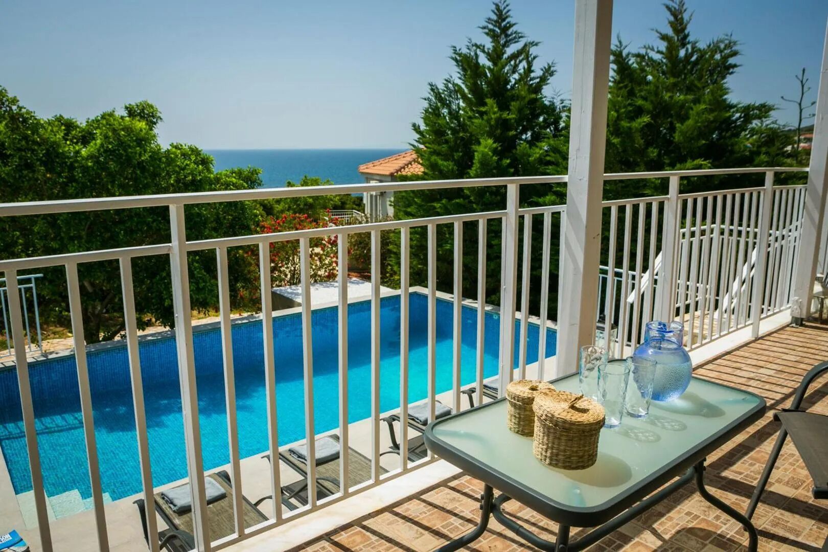 A poolside area with a glass table, wicker baskets, and a view of the sea.