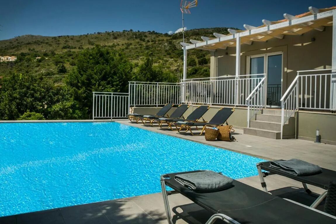 A swimming pool with lounge chairs, a pergola, and a view of a hillside.