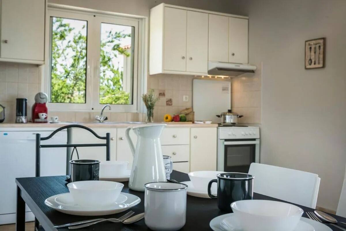 Una cocina con armarios blancos, una estufa y una ventana con vistas a plantas.