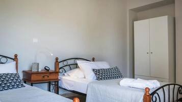 Una habitación con dos camas, un armario, una mesita de noche con lámpara y un pequeño mueble de madera.
