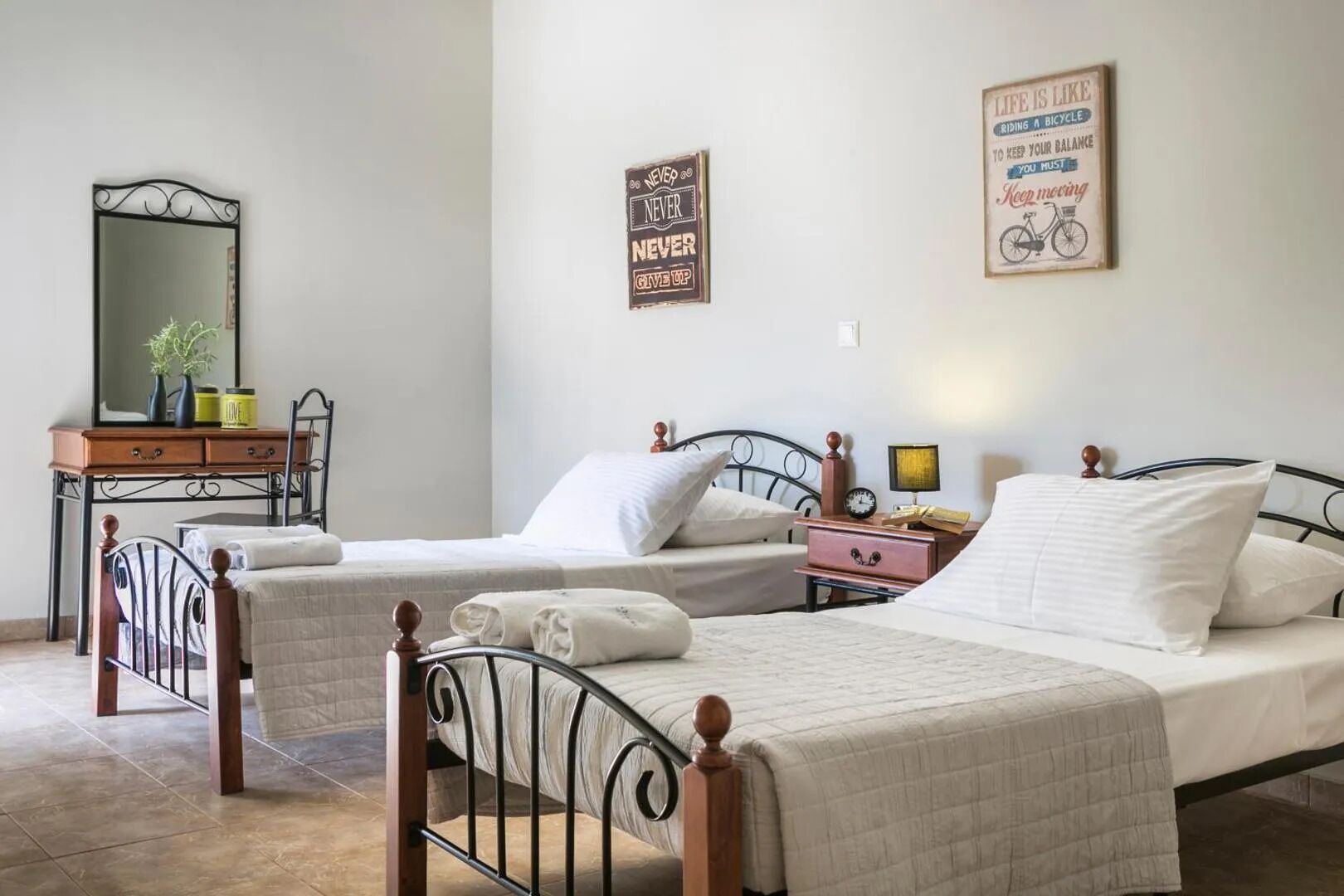 Ein Schlafzimmer mit zwei Einzelbetten, einem Schminktisch, einem Spiegel und Wandbildern.