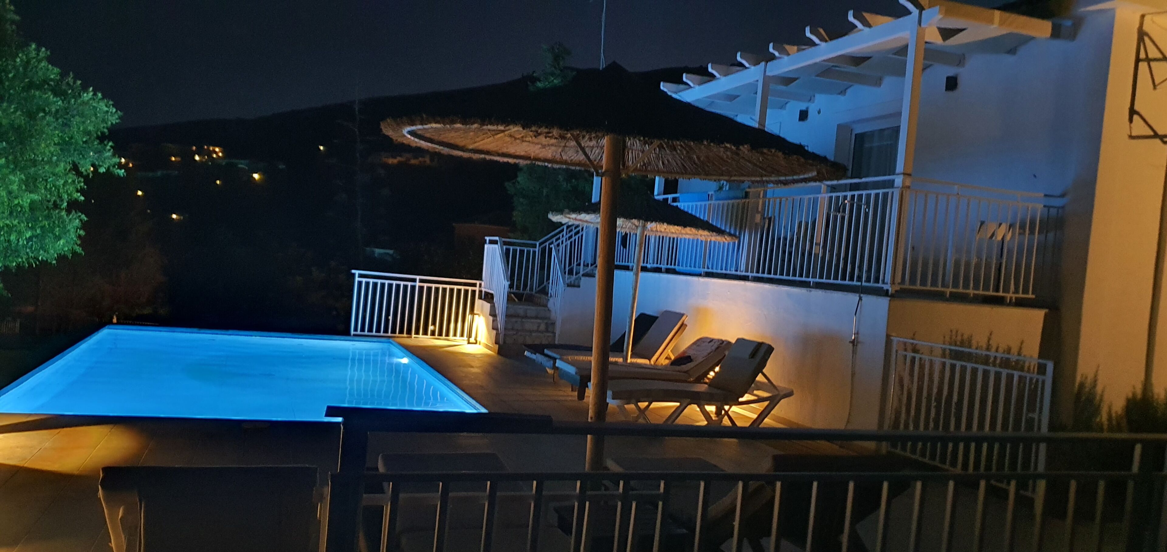 A swimming pool with a thatched umbrella, lounge chairs, and a white railing.