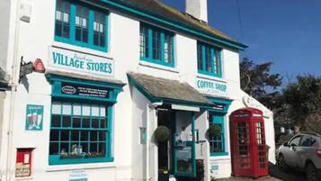 A white building with blue trim and a red telephone booth. It has signs for 'Village Stores' and 'Coffee Shop.'