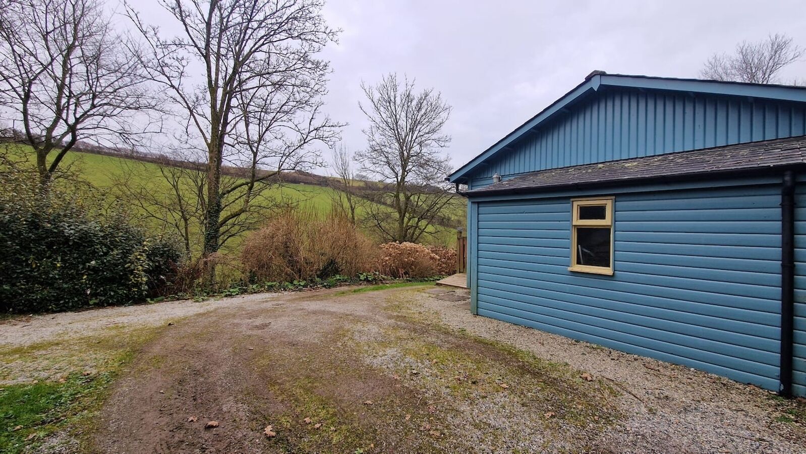 A blue building with a gravel driveway leading to a wooden door.