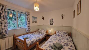 A room with two wooden beds, a window with curtains, a wall-mounted lamp, and a painting.