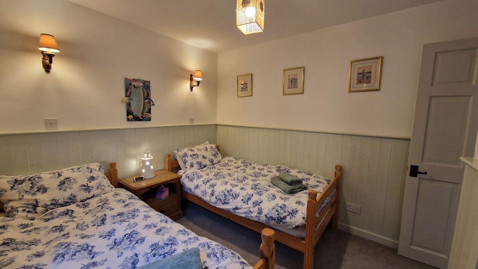 A room with two single beds, a nightstand with a lamp, and a door.