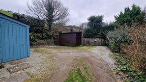 A gravel driveway leading to a blue shed and a brown structure, surrounded by dense vegetation and trees.