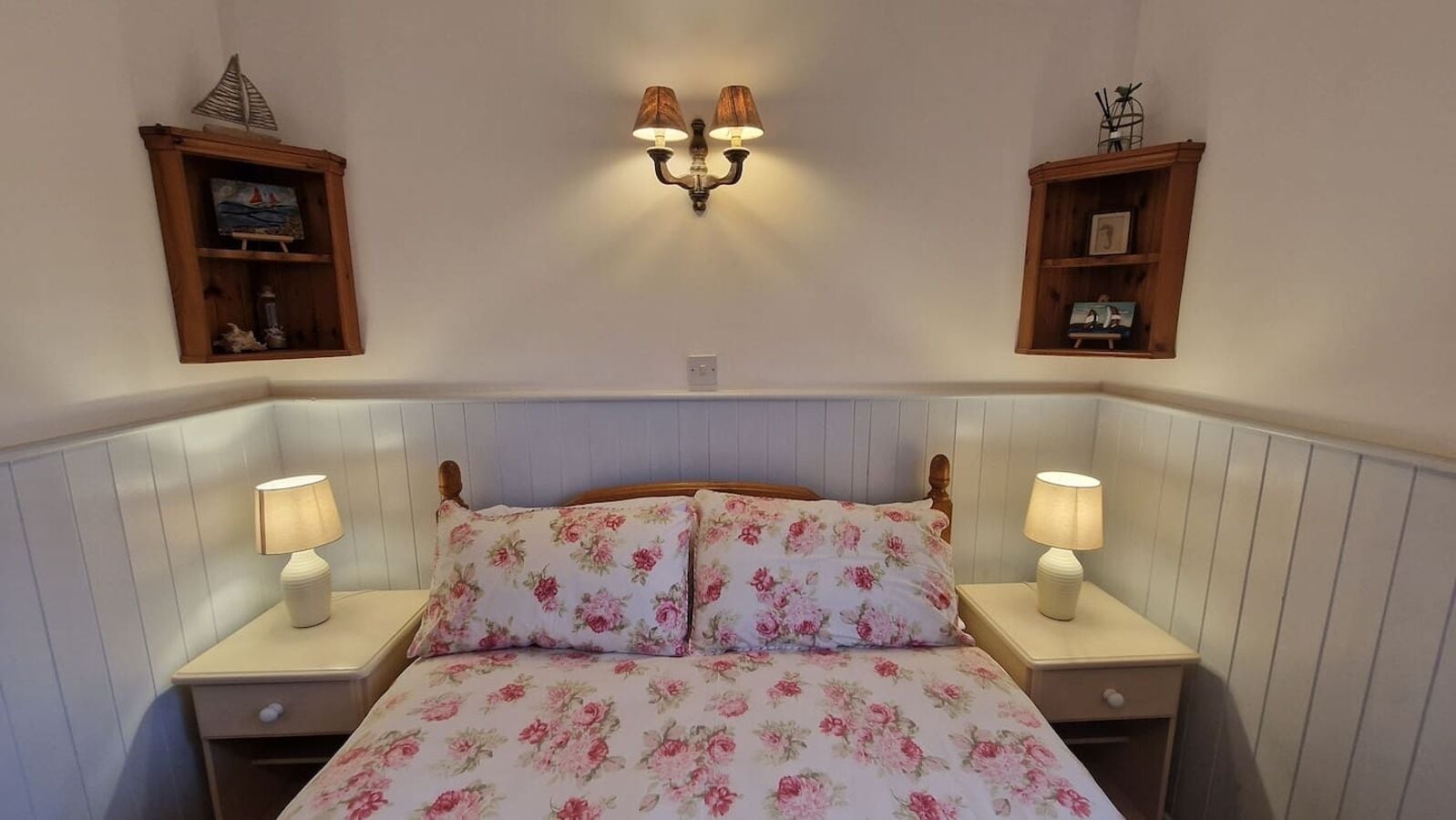 A bedroom with a floral bedspread, two bedside lamps, and wall-mounted sconces.