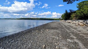 Pikkukivinen ranta, kirkas taivas ja kauempana näkyvät puut.