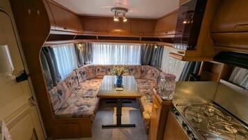 Interior compacto de una caravana con kitchenette, comedor y zona de estar.