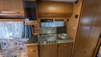 Una cocina compacta con estufa a gas, armarios de madera y una ventana con cortinas.