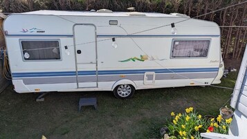 Una caravana blanca con una puerta lateral, una ventana pequeña y un diseño decorativo en el costado.