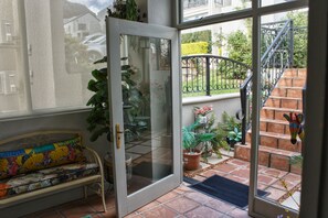 Une porte vitrée donnant sur un balcon agrémenté de plantes en pot, d’un banc et d’un escalier.