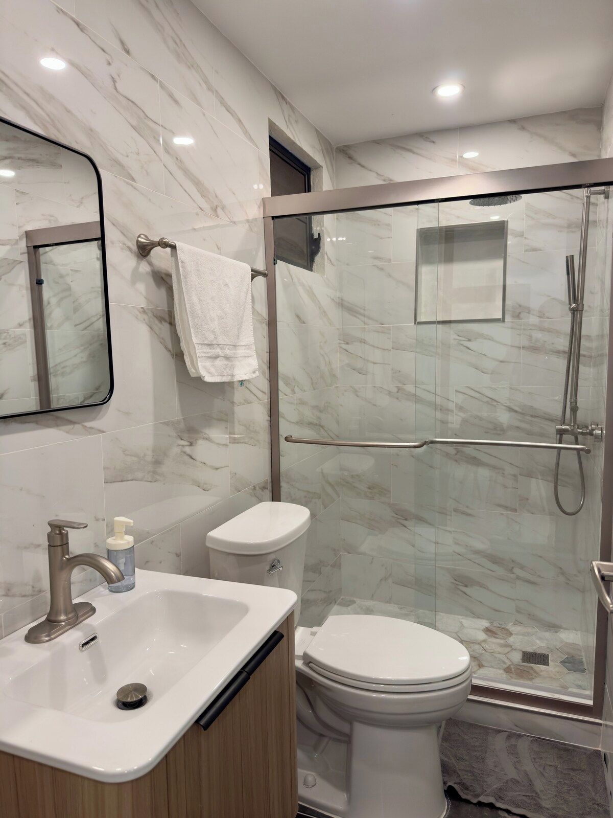 Une salle de bain moderne avec une douche à parois de verre, des toilettes et un lavabo surmonté d’un miroir.