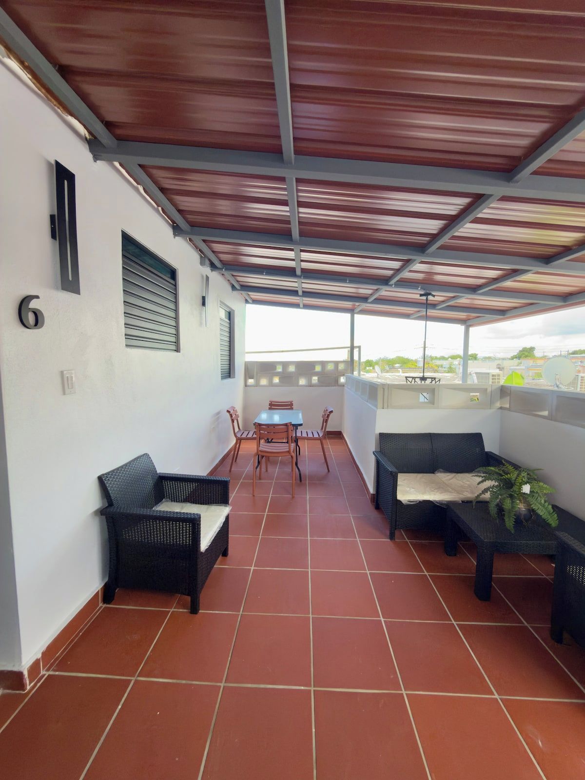 Eine überdachte Terrasse mit Fliesenboden, einem Tisch mit Stühlen und zwei Sofas.