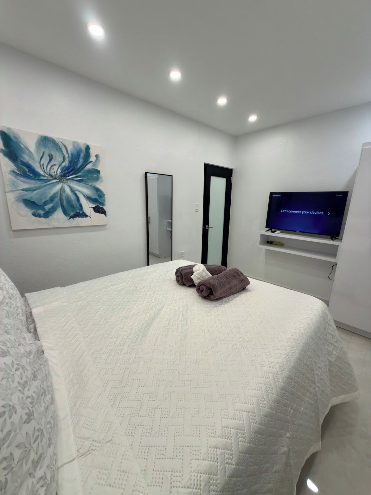 Ein Hotelzimmer mit einem Bett, einem Flachbildfernseher, einem Gemälde und einem Spiegel.