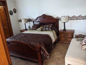 Un dormitori amb un llit de fusta, dues taules de nit amb làmpades, un aparador i una taula de nit amb una làmpada.