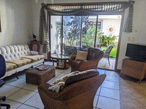 A living room with a sofa, two wicker chairs, a coffee table, and a television. - Delightful 4-bedroom house in Escazú, perfect for your getaway or business trip. (Escazú)