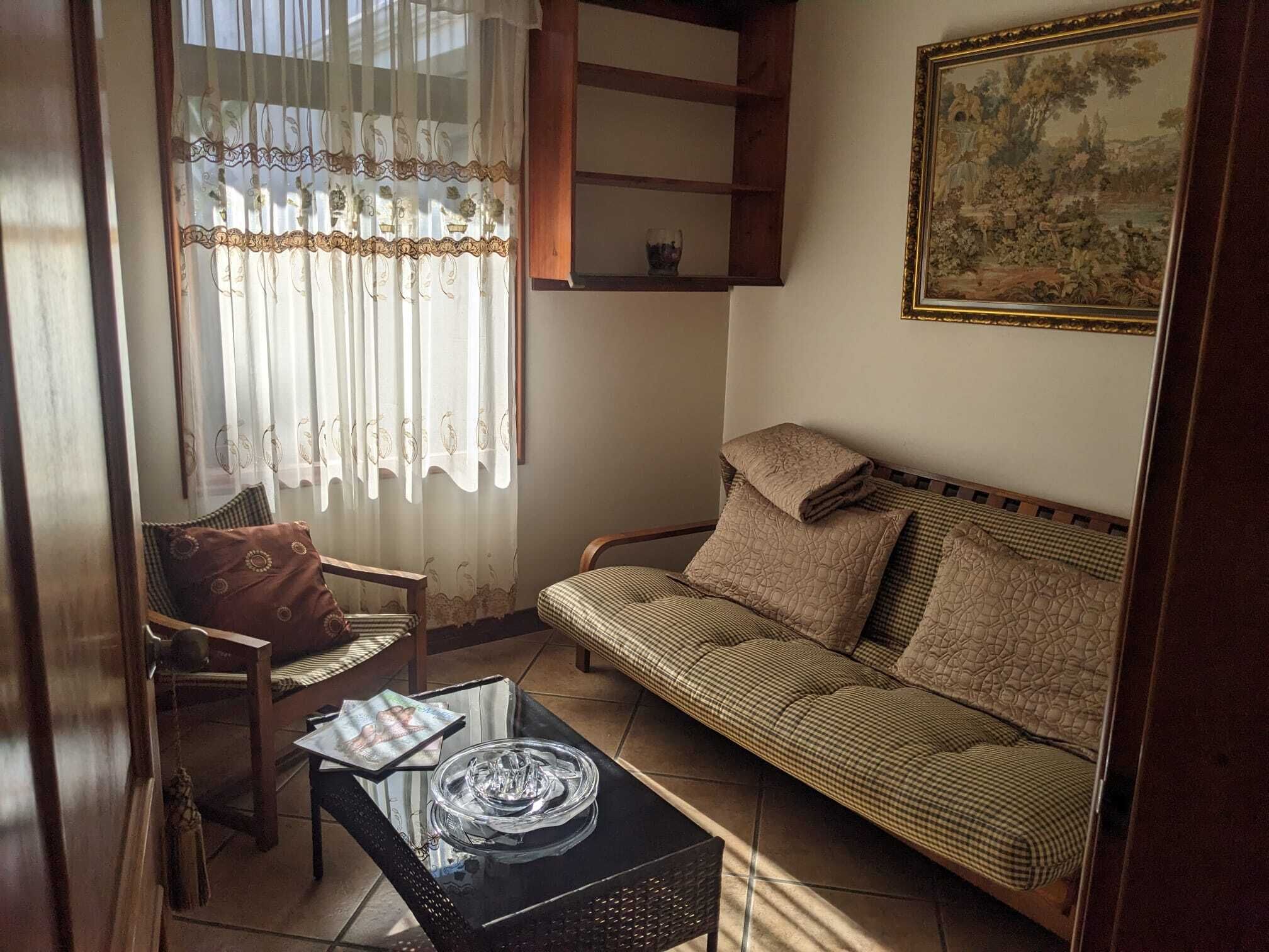 Uma sala de estar com sofá, poltrona, mesa de centro e um quadro na parede.