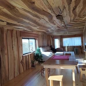 L’intérieur d’une cabane avec des murs en bois, un canapé, un petit sapin de Noël et une table à manger.