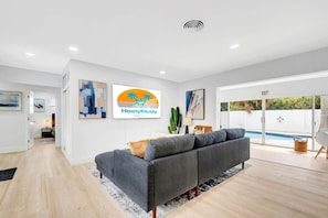 A modern living room with a grey sofa, a flat-screen TV, and a pool view. - Private Hollywood Oasis, Heated Pool, Spa and BBQ (Hollywood)