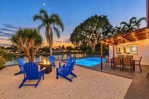 Un espace aménagé au bord de la piscine, avec des fauteuils Adirondack bleus, un foyer et une table à manger avec des chaises.