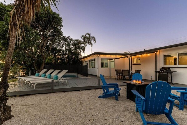 Un espace aménagé au bord de la piscine, avec des chaises longues, un foyer et des sièges d’extérieur.