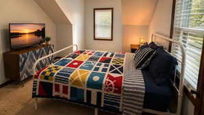 Une chambre à coucher comprenant un lit, un téléviseur, une fenêtre avec des stores et un luminaire au plafond.