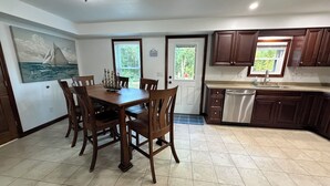 Une cuisine moderne avec des meubles de couleur bois foncé, un lave-vaisselle en acier inoxydable et un coin repas comprenant une table et des chaises en bois.