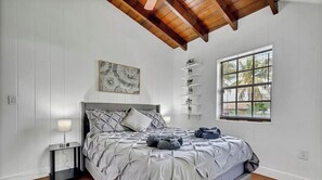 Une chambre à coucher comprenant un lit, une table de chevet, des œuvres d’art murales, une fenêtre et des étagères intégrées.