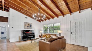 A spacious living room with a high ceiling, a fireplace, a sofa, and a large window. - 2-Home Compound with Pool and BBQ, Sleeps 16 (Miami)
