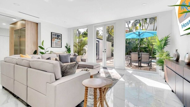 A modern living room with a sofa, a coffee table, and a dining area with outdoor seating. - Gated Miami Luxury Oasis Pool & BBQ I 4-Bed, 4-Bath (Miami)