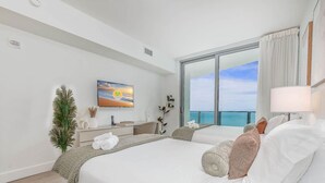 Una habitación de hotel moderna con una cama grande, un televisor, un balcón con vistas al mar y un pequeño escritorio con una planta.