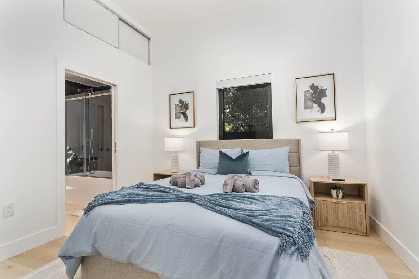 A bedroom with a bed, two bedside tables, a window, and a door leading to a bathroom.