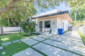 Ein modernes Haus mit befestigter Auffahrt, einem kleinen Garten und einer blauen Mülltonne.