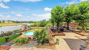 Une piscine avec un espace extérieur aménagé, une maison en pierre et une vue sur un lac.