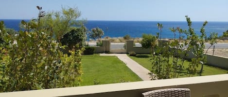 A balcony with wicker furniture, a view of the ocean, and a well-maintained lawn.