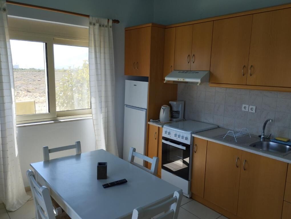 Ett kompakt kök med träskåp, en vit bänkskiva, en spis och ett fönster med gardiner.