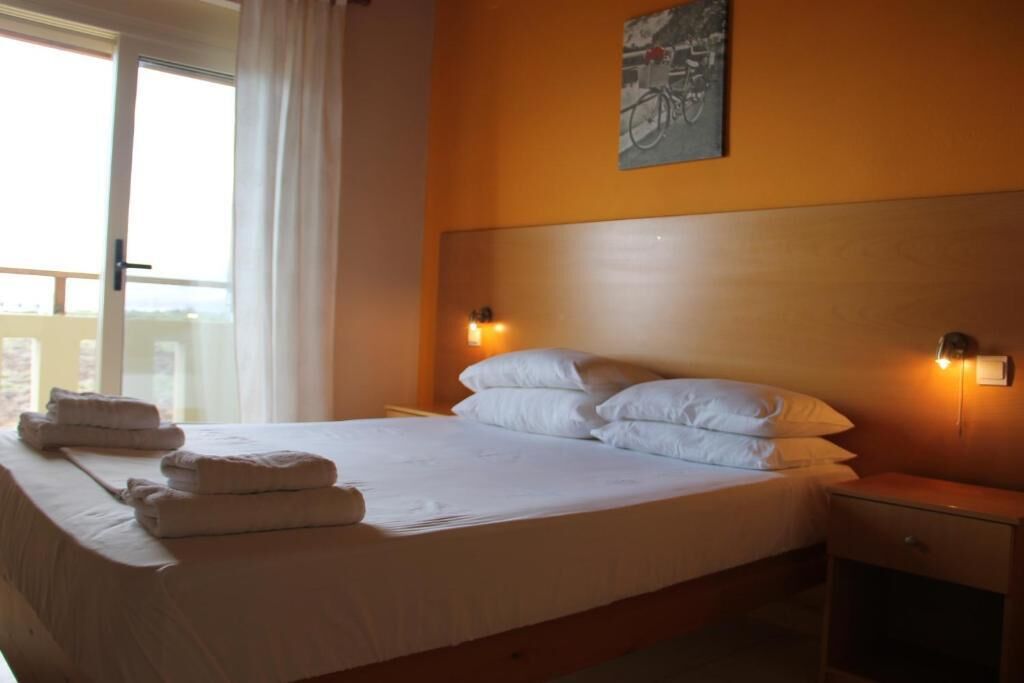 A bedroom with a bed, pillows, a nightstand, a wall-mounted light, and a window with curtains.