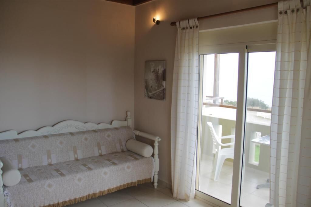 A room with a white sofa, a painting on the wall, and a sliding glass door leading to an outdoor area with chairs.