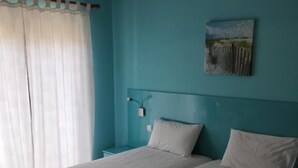 Een kamer met twee bedden, een nachtkastje, een lamp en een schilderij aan de muur.