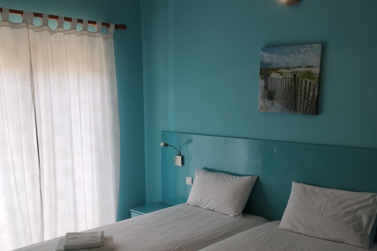 A room with two beds, a painting on the wall, and a window with curtains.