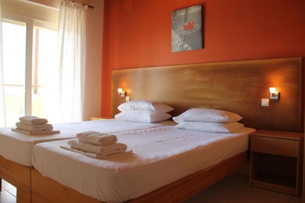 A hotel room with a large bed, two bedside tables, a headboard, and a window with curtains.