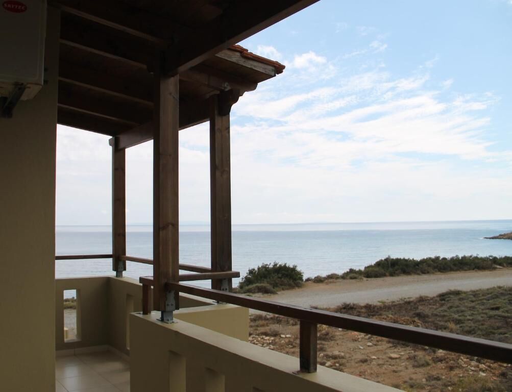 A covered outdoor area with a view of the sea, wooden pillars, and a tiled floor.