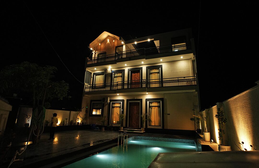 Un edificio de dos pisos con piscina, balcones e iluminación exterior.