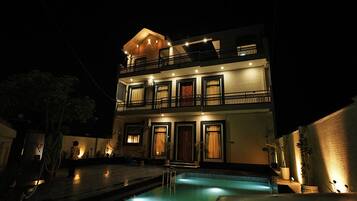 Un edificio de dos pisos con piscina, balcones e iluminación exterior.