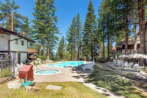Ein Poolbereich mit Liegestühlen, einer Holzterrasse und umliegenden hohen Kiefern.